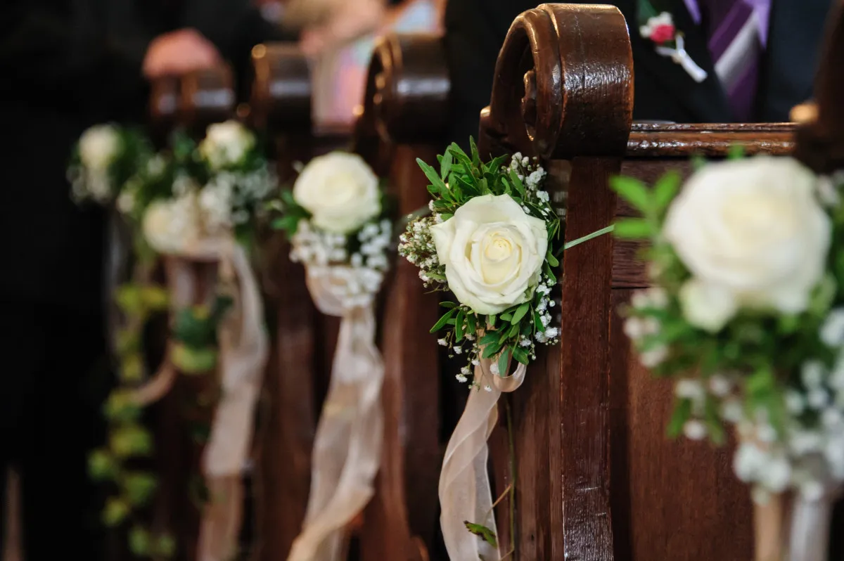 Composizioni di rose bianche e gipsofila sui banchi della chiesa per un matrimonio