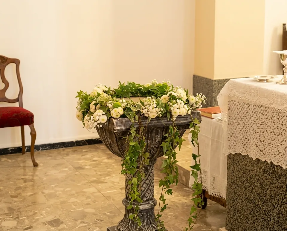 Fonte battesimale in pietra decorata con fiori bianchi, crisantemi verdi ed edera ricadente accanto all'altare di una chiesa, preparata per un battesimo